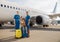 Full length shot of happy two kids sitting on their luggage in front of big airplane on a daytime and smiling at camera