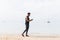 Full Length Shot Of Male Runner Using Cell Smart Phone On Beach While Jogging On Seaside Man Young Latin Sport