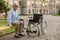 Full length shot of mature recovering patient with wheelchair sitting on the bench in the park near clinic