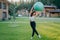 Full length shot of serious slim brunette woman has perfect body shape holds fitness ball over head, does fitness exercises
