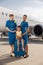 Full length shot of smiling beautiful stewardesses standing near cute little girl sitting on suitcase in front of big