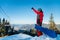 Full length shot of a snowboarder standing on the top of the mountains, showing thumb up, enjoying beautiful winter day
