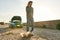 Full length shot of young man looking frustrated, talking on the phone with car service, assistance or tow truck while