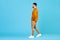 Full length side profile of young male walking, stepping, looking at empty space isolated on blue color background