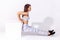 Full length side view assertive sportive woman in white top and tights pumping abs muscles doing sit ups, exercising with cube