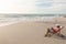 Full length side view of biracial senior man using digital tablet relaxing on folding chair at beach