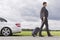 Full length side view of young businessman with luggage leaving broken down car at countryside