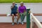 Full length of tired biracial senior couple drinking water while sitting on bench at tennis court