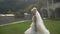 FUll-length view of th attractive blonde bride in long stylish wedding dress running along the garden during the sunset.