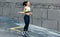 Full-length view of young determined woman skipping with a rope outdoors next to the concrete wall. Fitness female exercising with