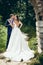 Full-length wedding portrait of the groom tenderly kissing his lovely bride with open back in cheek in the green forest