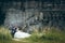 Full-length wedding portrait of the stylish happy newlyweds tenderly holding hands while sitting on the old castle