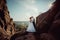 Full-length wedding shot of the stylish newlywed couple softly kissing on the mountains at the background of the