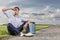 Full length of young man shielding eyes while sitting with petrol can by country road