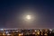 Full moon on colorful night sky above city lights