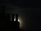 The full moon hides behind the chimneys in a misty night sky