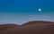 Full moon over sand dunes in sahara desert