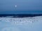 Full moon over the snow-covered slope of the polar hill in winter with a distant view of Kandalaksha, port city in northern Russia