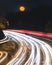 Full moon rising above a curving highway. Light trails from cars speeding by