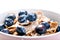 Full muesli bowl on a white table with blueberry and milk splash. Healthy breakfast cereals with milk, seed, fruit. Oat flakes