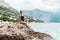 Full relaxation. woman in body swimsuit sitting on a rock at seaside with mountains in background