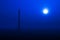 Full shiny moon on the dark clear blue sky over the meadow and lonely electric current pillar