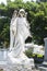 Full size adult female angel with flowers in cemetary with trees and over graves behind her