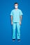 Full size fullbody portrait of attractive handsome man in sterile mask and blue lab suit, looking at camera, isolated on