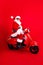 Full size photo of astonished funny grandfather wear trendy santa costume glasses riding fast on moped isolated on red