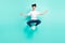 Full size photo of calm brunet hairdo teenager guy jump do yoga wear t-shirt jeans isolated on teal background