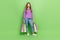 Full size photo of cheerful girl with long hairstyle dressed jeans purple pullover hold shopping bags isolated on green
