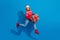 Full size photo of cheerful schoolgirl dressed red sweater santa running shopping with gift on new year isolated on blue