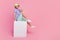 Full size photo of handsome young guy sit blank banner cube shopping promo dressed trendy blue garment isolated on pink