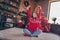 Full size photo of hooray young lady sit on floor near gifts tree wear red sweater jeans socks at home alone on new year