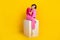 Full size photo of optimistic girl dressed knitwear top pink pants look empty space sitting on cube isolated on yellow