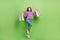 Full size photo of positive cheerful girl dressed jeans purple pullover hold shopping bags jumping isolated on green