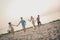 Full size photo of positive cheerful hippie youngsters fellows guys ladies run sand coastline hold hands outside