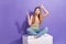 Full size photo of pretty teenager blonde girl sit cube point empty space wear trendy striped outfit isolated on purple