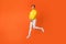 Full size photo of pretty teenager moving jumping looking have smile on her face isolated over orange background