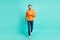 Full size photo of young handsome cheerful man go walk travel wear orange sweater isolated on turquoise color background