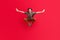 Full size photo of young smiling attractive guy jumping hands wings flying freedom isolated on red color background