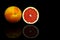 Full and sliced grapefruits on reflective dark background