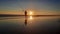 From full sun at sunset silhouetted fisherman with his very long rod on reflecting wet beach sand