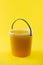 Full transparent bucket with bee honey on a yellow background