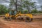 Full view of a road grader machine, leveling the ground with person to drive