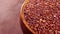 Full wooden bowl of raw red quinoa seeds on a wood surface.