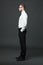 Fullbody profile view of handsome businessman on dark gray background.