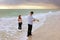 Fully clothed couple standing in ocean at sunset