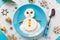 Fun food idea for kids. Christmas children`s Breakfast: snowman of cottage cheese on a blue plate.