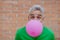 Fun portrait of happy energetic mature man inflating pink balloon in street, standing in front of brick wall, copy space
